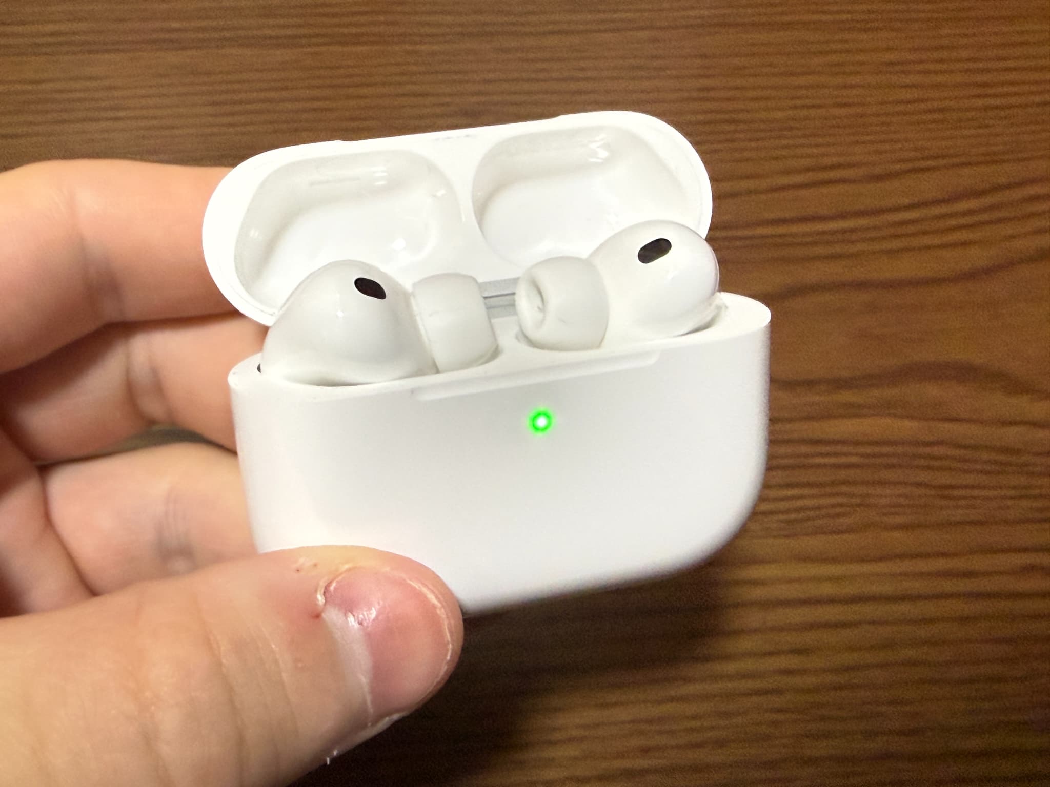 指で持たれた充電ケースが開いた状態のワイヤレスイヤホン