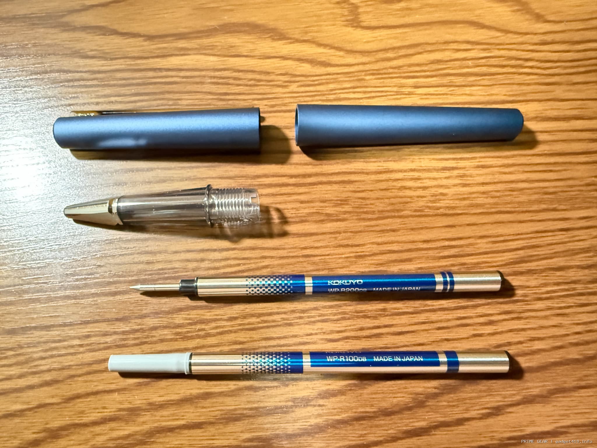 木の机の上に置かれた分解された青いコクヨのボールペンと替え芯